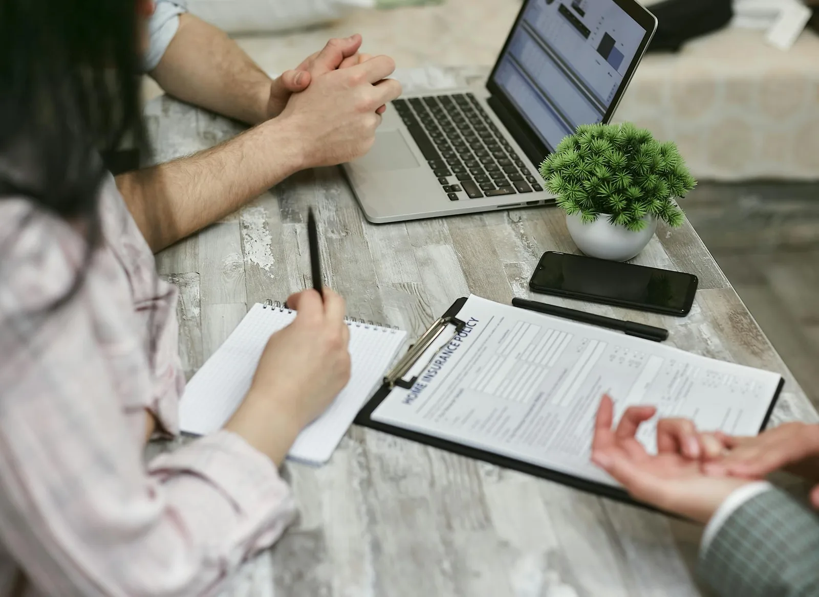 People discussing home insurance policy documents at a workspace with laptop and phone